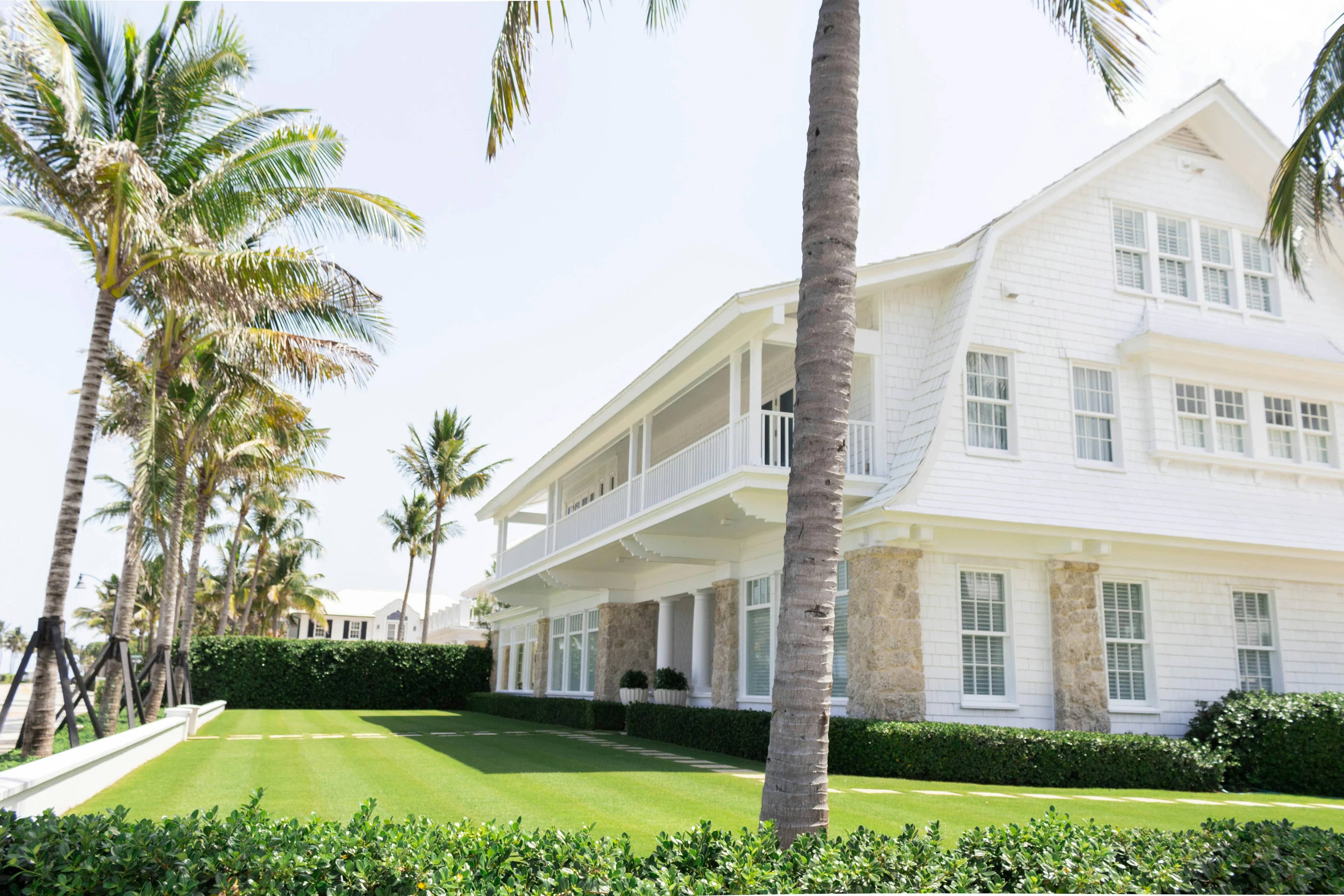 White two-story home framed by palm trees and a manicured lawn
